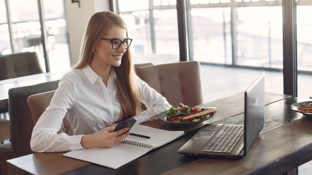 Empreendedora trabalha no notebook e no celular em um café, rotina de franqueados sem ponto físico